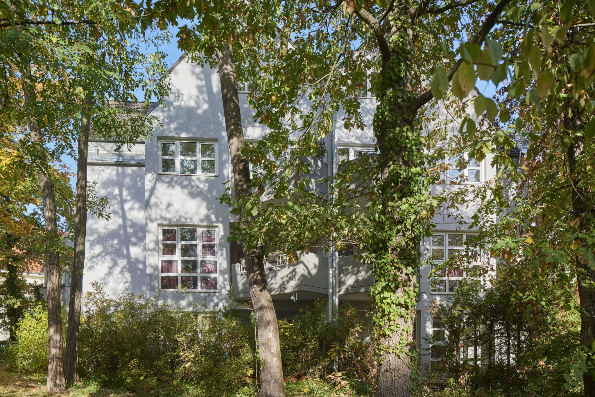 weißes Haus zwischen Bäumen der Wohnanlage Jagdfeld RE Living in Berlin Grunewald